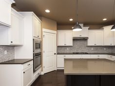 an empty kitchen with white cabinets and black counter tops is seen in this image, there are two pendant lights hanging over the island