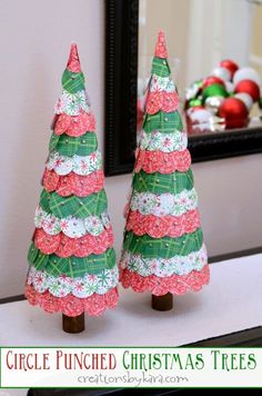 two christmas trees made out of paper on top of a table next to a mirror