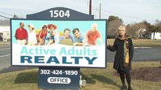 a woman standing in front of a sign for active adults realty with people on it