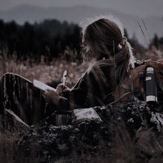 a woman is sitting in the grass with her cell phone and looking at something she's holding