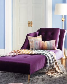 a purple chaise lounge chair with pillows on it in a blue and white room