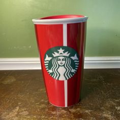 a red starbucks cup sitting on top of a wooden table next to a green wall