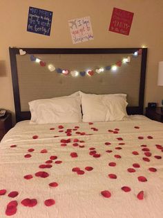 a bed with white sheets and red rose petals on the headboard, along with string lights