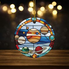 a stained glass ornament depicting the solar system on a wooden table with lights in the background