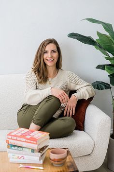 a woman sitting on a couch with books and a potted plant in the corner