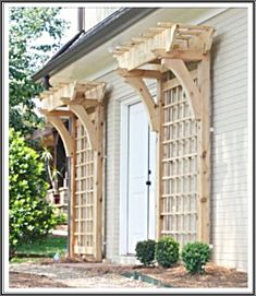 an outdoor wooden arbor with trelliss on the side of a white house in front of a tree