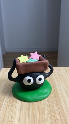 a cake shaped like a pot with eyes and stars on it's top sitting on a wooden table