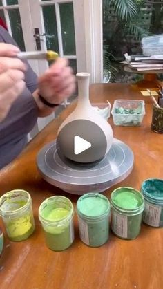 a person holding a paintbrush in front of some cups and containers on a table