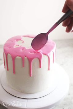 a white cake with pink icing being drizzled onto it by a spoon