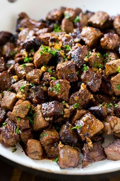 a white bowl filled with cooked meat and garnished with parsley on top