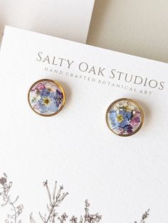 a pair of earrings sitting on top of a white card next to some plants and flowers