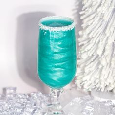 a glass filled with blue liquid next to a white christmas tree