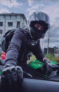 a man in black jacket and helmet sitting on green motorcycle