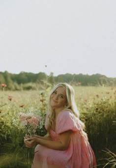 a woman in a pink dress sitting on the ground with flowers and grass behind her