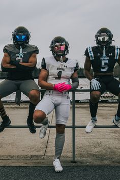 three football players sitting on a fence with their arms around each other and wearing helmets