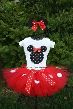 a red and white minnie mouse tutule outfit with polka dots on it, sitting in front of some bushes