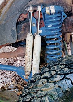 the front suspensions and tires of an old car are exposed in muddy mud, with leaves on the ground below