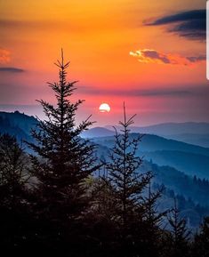 the sun is setting over mountains and trees