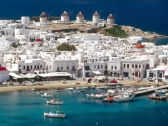 boats are docked in the blue water near white buildings and windmills on an island