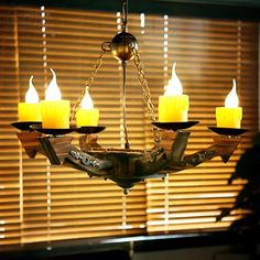 a chandelier with five lit candles hanging from it's sides in front of a window