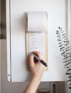 a person writing on a piece of paper with a pen and clipboard attached to the wall