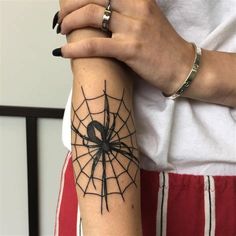 a woman holding her arm with a spider tattoo on it's left arm and wrist