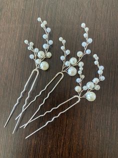 three hair pins with pearls on them sitting on top of a wooden table next to each other