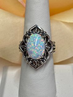 Simulated Opal Gemstone Ring  Oval Mesh Design#98 Custom Made This is a lovely Gothic inspired sterling silver filigree ring.  The stunning rainbow white simulated opal is 14mmx 10mm in length and width.  The setting is 24mm North/South on the finger.  The inside of the band is marked 925 for sterling silver. The filigree has a subtle floral design that accents the dazzling center stone.  This unusual gothic ring is  an amazing mixture of sophisticated style combined with an expressive elegance. Classic Oval Opal Jewelry, Formal Oval Opal Ring In Sterling Silver, Oval Opal Ring With Stone Setting For Formal Occasions, Formal Oval Opal Ring With Stone Setting, Elegant Adjustable Opal Ring, Ornate Oval White Gold Filigree Ring, Ornate Oval Cabochon Jewelry, Adjustable Oval Opal Ring In White Gold, Adjustable Oval Cabochon Opal Ring