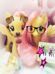 two little ponys with pink hair and glasses next to each other on a table