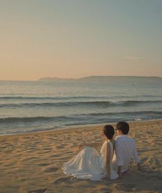 two people sitting on the beach looking at the ocean