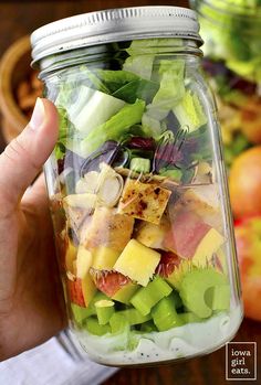 a person holding up a mason jar filled with fruit and veggie salads