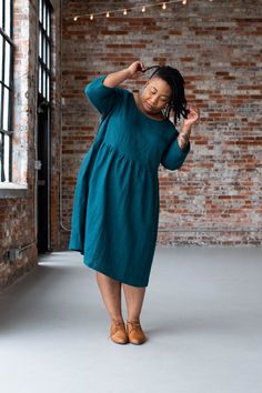 a woman in a blue dress standing by a brick wall with her hand on her head