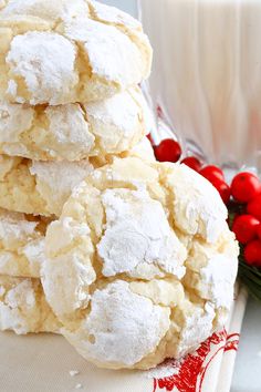 a stack of powdered sugar cookies next to a glass of milk and holly berries