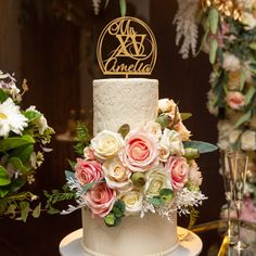 a wedding cake decorated with flowers and a gold monogrammed name on the top