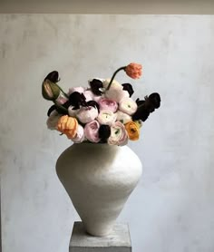 a white vase filled with lots of different colored flowers on top of a cement block