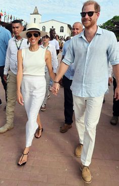 a man and woman walking down a sidewalk holding hands with other people in the background