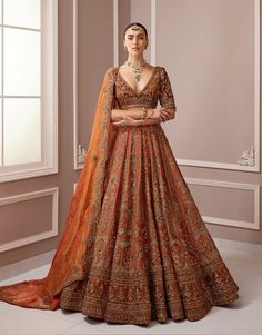 a woman in an orange and gold lehenga is standing with her arms crossed