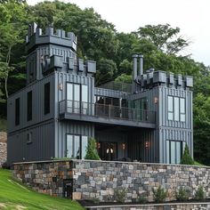 a large gray house sitting on top of a lush green hillside next to a forest