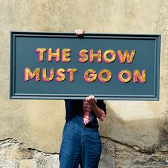 a man holding up a sign that says the show must go on in front of him