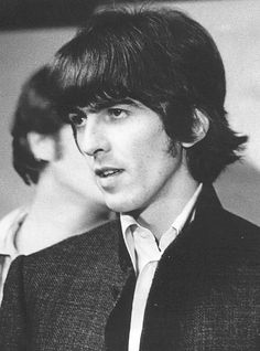 black and white photo of young man with long hair in suit jacket looking at camera