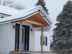 a small white house covered in snow next to trees