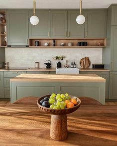 a bowl of fruit sitting on top of a wooden table next to a kitchen counter