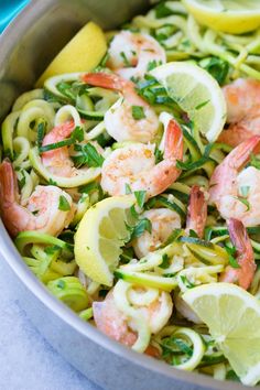 shrimp and zucchini pasta in a pan with lemon wedges