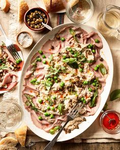 a platter filled with meat and vegetables on top of a table next to bread