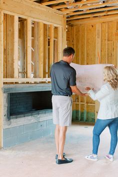 a man and woman standing in front of a house under construction looking at blueprint