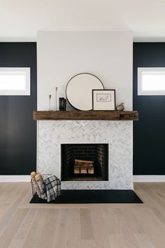 a white fireplace with black walls and wood flooring in the living room, along with a round mirror above it