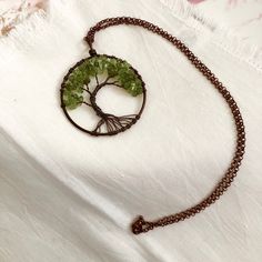 a necklace with a tree on it and a chain hanging from the front, sitting on a white cloth