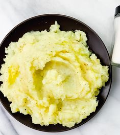 mashed potatoes in a black plate next to a glass of milk on a marble surface