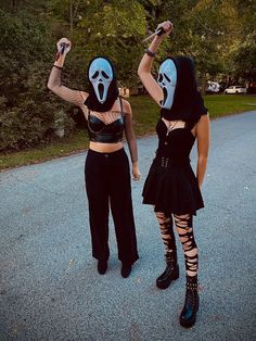 two women dressed in costumes are walking down the street with their hands up and one is wearing a mask