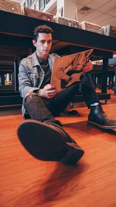 a young man sitting on the floor reading a book with his feet propped up in front of him